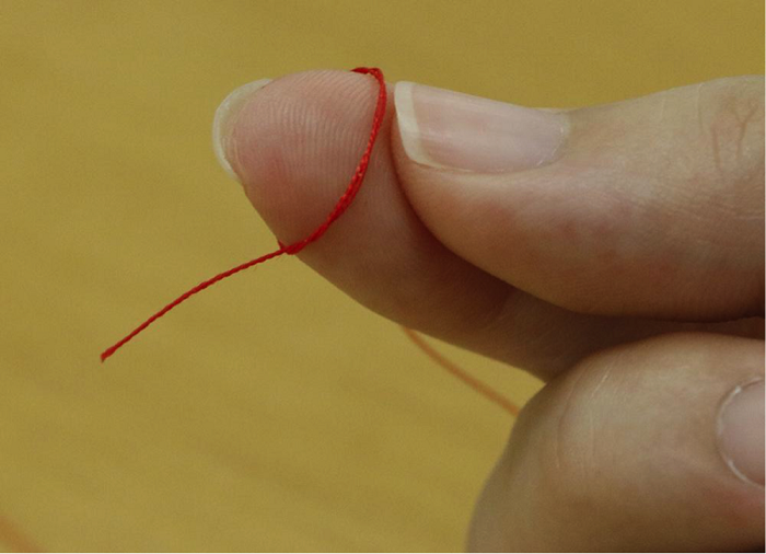 2.親指で糸の端を上に折り上げます。