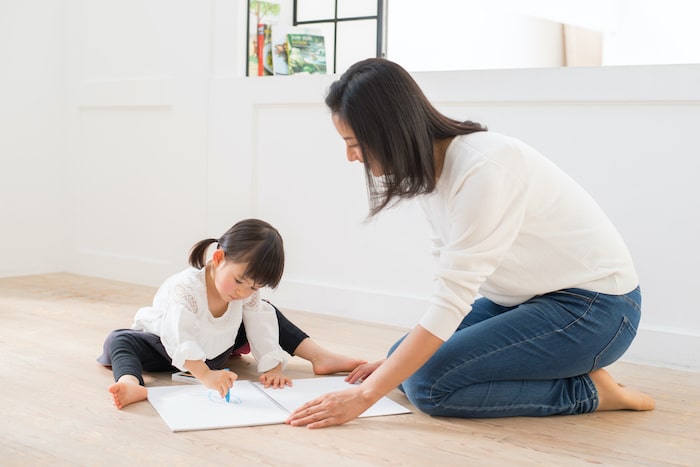 大人と一緒に床でお絵描きをする子供