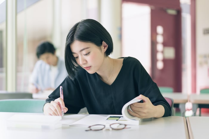 眼鏡を机の上に置いてテキストを使って勉強する女性