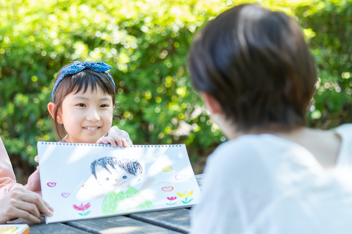 クレヨンで書いた絵を母親に見せる少女